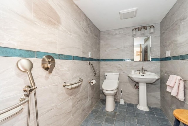 bathroom with toilet, tile patterned flooring, tile walls, and sink