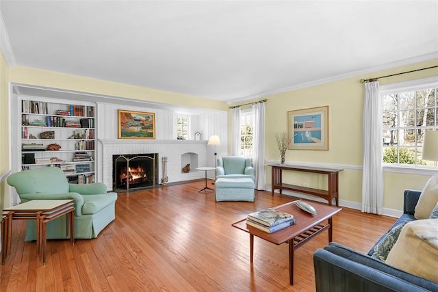 living area with baseboards, wood finished floors, a fireplace, and ornamental molding