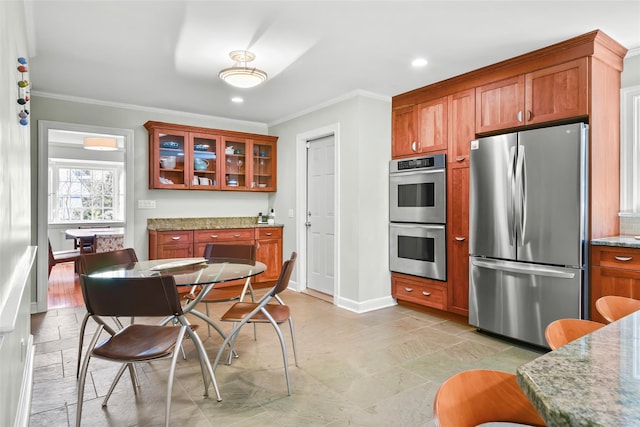 kitchen with light stone countertops, baseboards, stainless steel appliances, crown molding, and brown cabinets