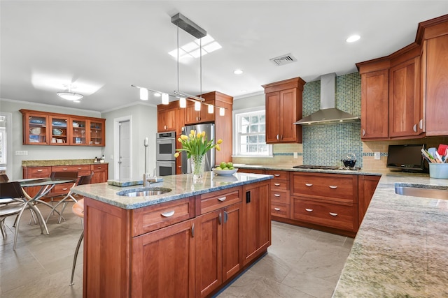 kitchen featuring a center island, light stone countertops, appliances with stainless steel finishes, wall chimney exhaust hood, and a sink