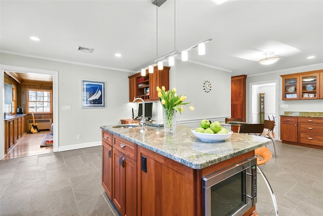 kitchen with a sink, stainless steel microwave, light stone countertops, and crown molding