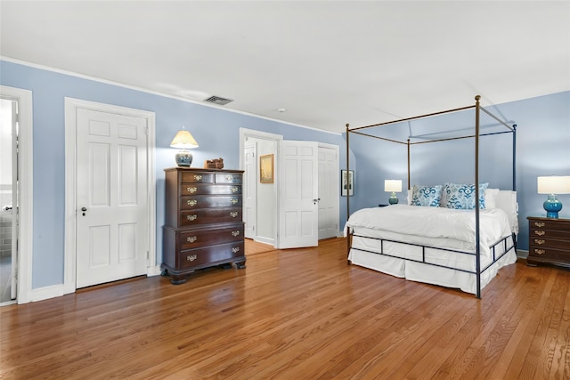 bedroom with visible vents, baseboards, wood finished floors, and ornamental molding