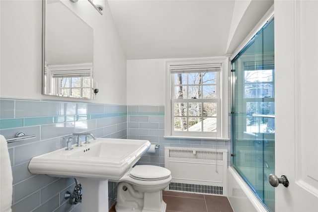 full bathroom featuring lofted ceiling, radiator heating unit, tile patterned floors, toilet, and tile walls