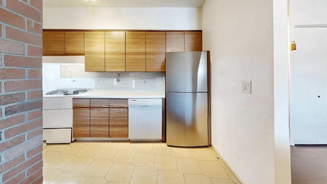 kitchen with freestanding refrigerator, light countertops, dishwasher, brown cabinets, and backsplash