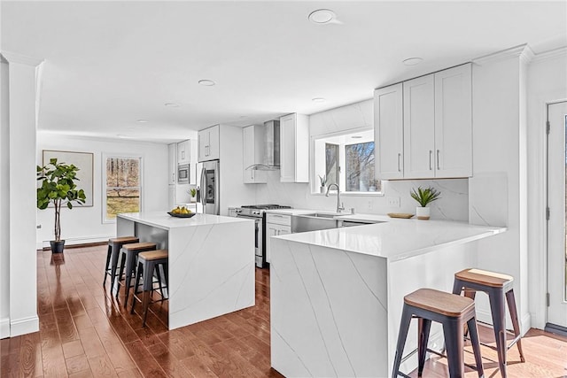 kitchen with wall chimney range hood, sink, appliances with stainless steel finishes, a kitchen bar, and a kitchen island