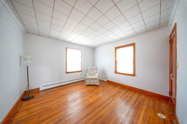 unfurnished room featuring hardwood / wood-style flooring, a healthy amount of sunlight, a baseboard heating unit, and crown molding