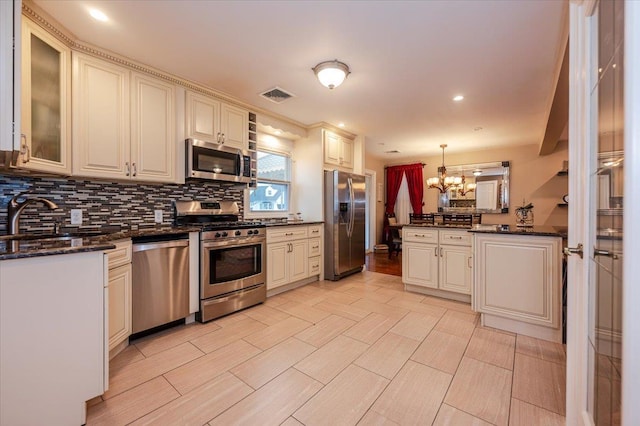 kitchen featuring sink, an inviting chandelier, hanging light fixtures, appliances with stainless steel finishes, and dark stone counters