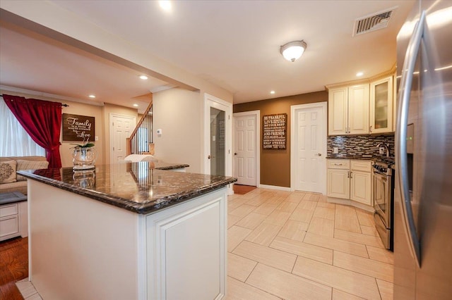 kitchen featuring appliances with stainless steel finishes, decorative backsplash, dark stone counters, a kitchen island, and cream cabinets