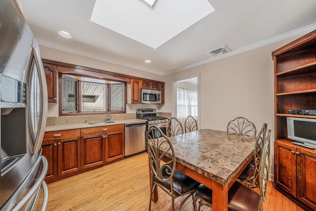 kitchen with sink, crown molding, a skylight, light wood-type flooring, and appliances with stainless steel finishes