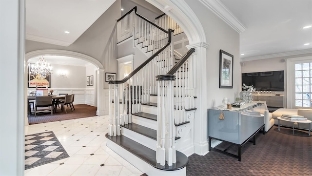 staircase with decorative columns, ornamental molding, and a notable chandelier