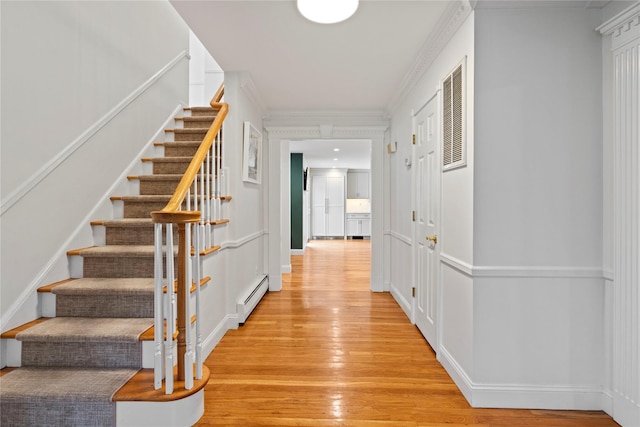 interior space with a baseboard heating unit, light hardwood / wood-style flooring, and crown molding