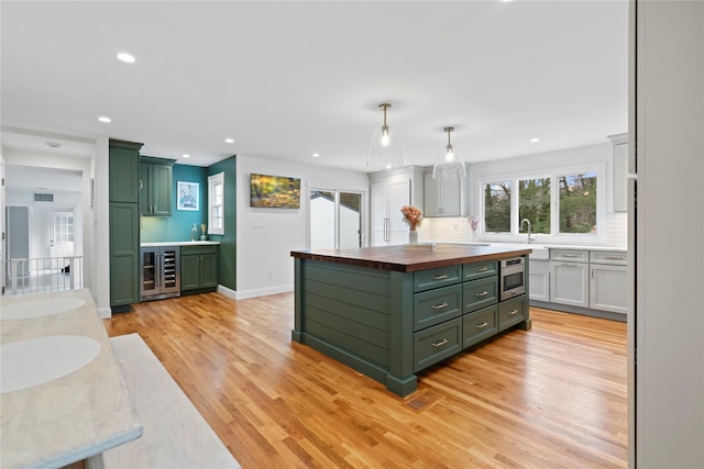 kitchen with decorative light fixtures, stainless steel microwave, green cabinets, light wood-type flooring, and wood counters