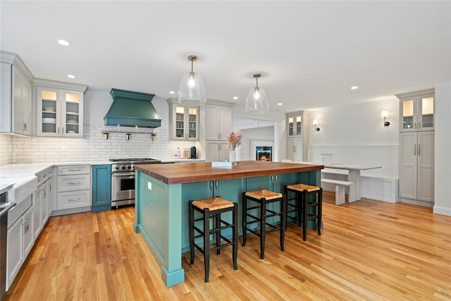 kitchen with high end stainless steel range, premium range hood, a kitchen breakfast bar, hanging light fixtures, and butcher block countertops