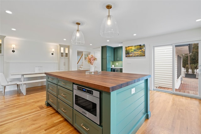 kitchen featuring stainless steel microwave, a center island, pendant lighting, butcher block countertops, and green cabinetry