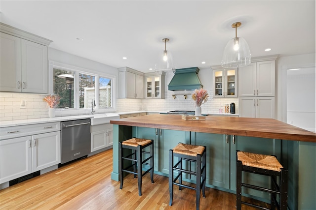 kitchen with decorative light fixtures, custom exhaust hood, butcher block countertops, a kitchen bar, and appliances with stainless steel finishes