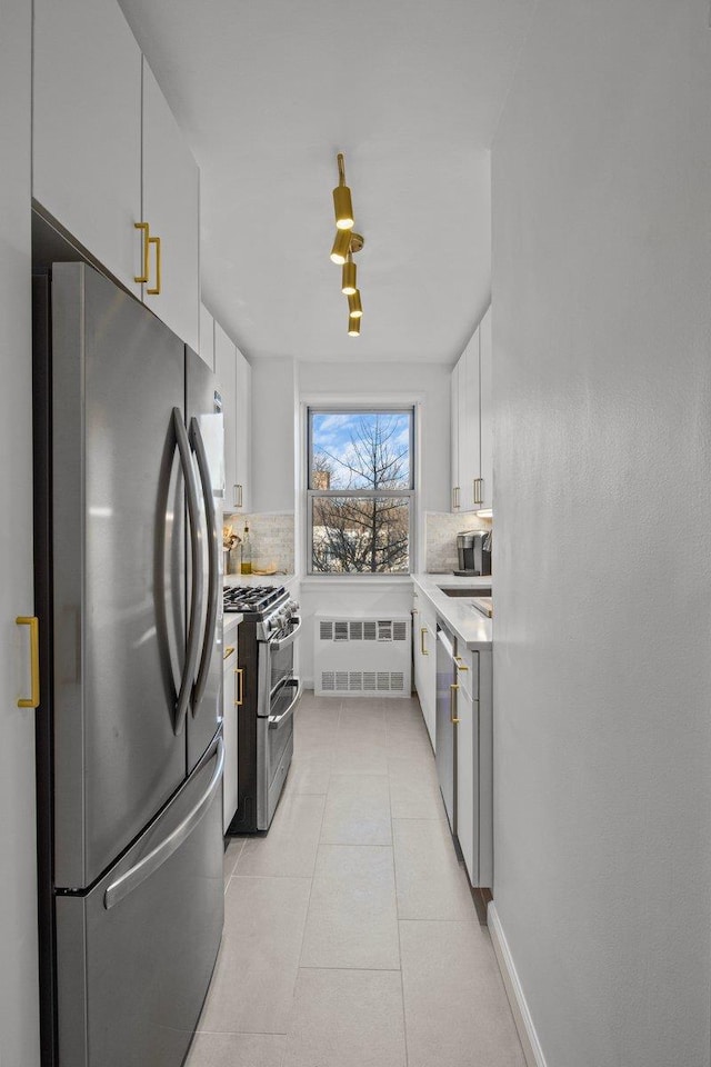 kitchen with appliances with stainless steel finishes, tasteful backsplash, white cabinetry, radiator, and light tile patterned floors