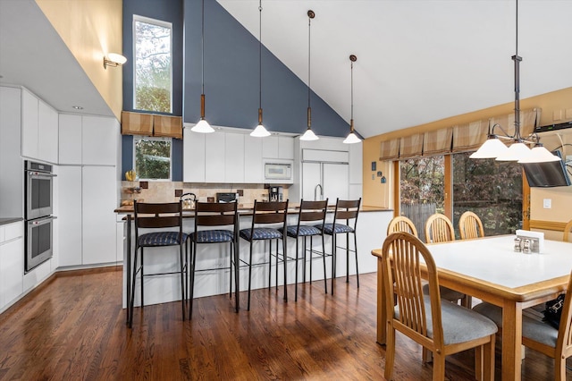 interior space featuring white cabinetry, decorative backsplash, high vaulted ceiling, hanging light fixtures, and built in appliances