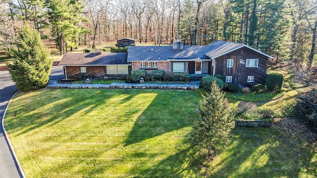 ranch-style home with a forest view, a chimney, and a front lawn