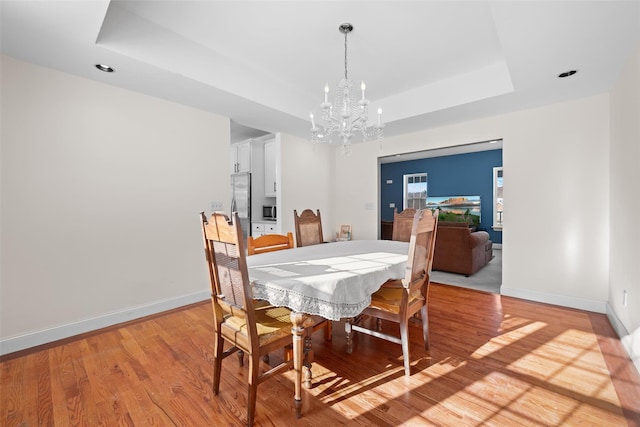 dining room with an inviting chandelier, a tray ceiling, and light wood-type flooring