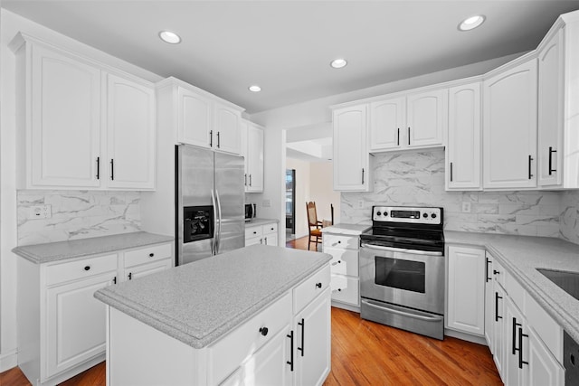 kitchen featuring white cabinetry, light wood-type flooring, a kitchen island, stainless steel appliances, and backsplash