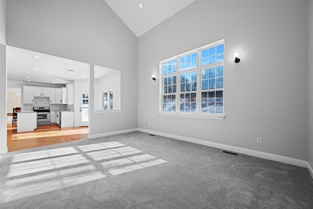 unfurnished living room with light colored carpet and high vaulted ceiling