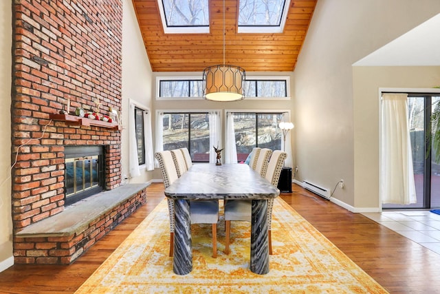 dining area featuring a skylight, high vaulted ceiling, a brick fireplace, hardwood / wood-style flooring, and a baseboard heating unit