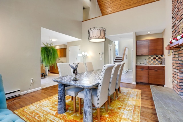 dining space with a high ceiling, baseboard heating, and light hardwood / wood-style floors