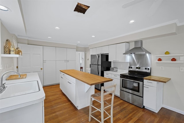 kitchen with white cabinets, appliances with stainless steel finishes, wall chimney range hood, ornamental molding, and light wood-type flooring