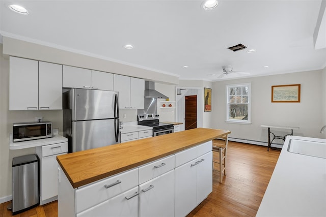 kitchen with appliances with stainless steel finishes, white cabinets, a kitchen island, wall chimney range hood, and sink