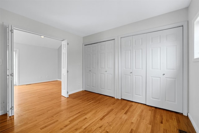 unfurnished bedroom with multiple closets and light wood-type flooring