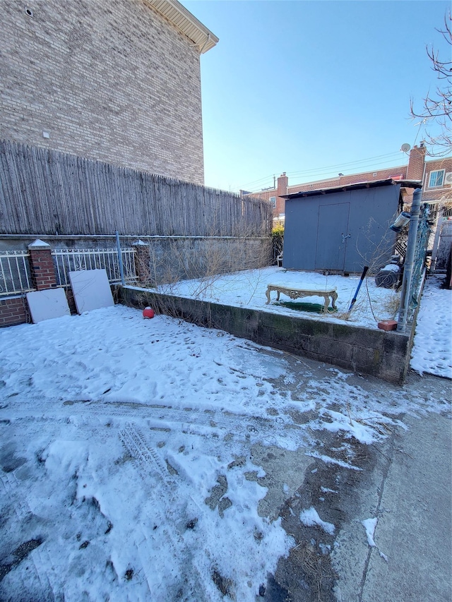 yard covered in snow featuring a storage unit, an outdoor structure, and fence