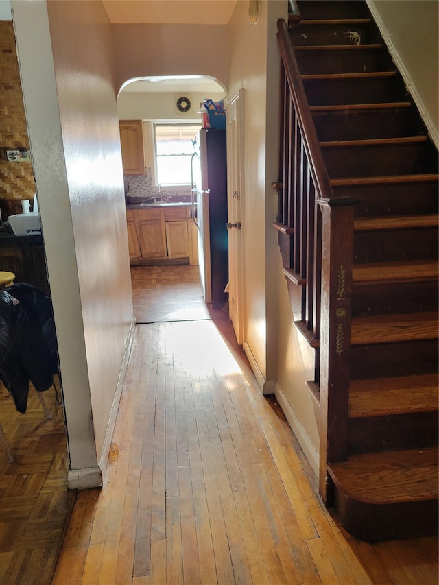 hall featuring baseboards, stairway, light wood-type flooring, arched walkways, and a sink