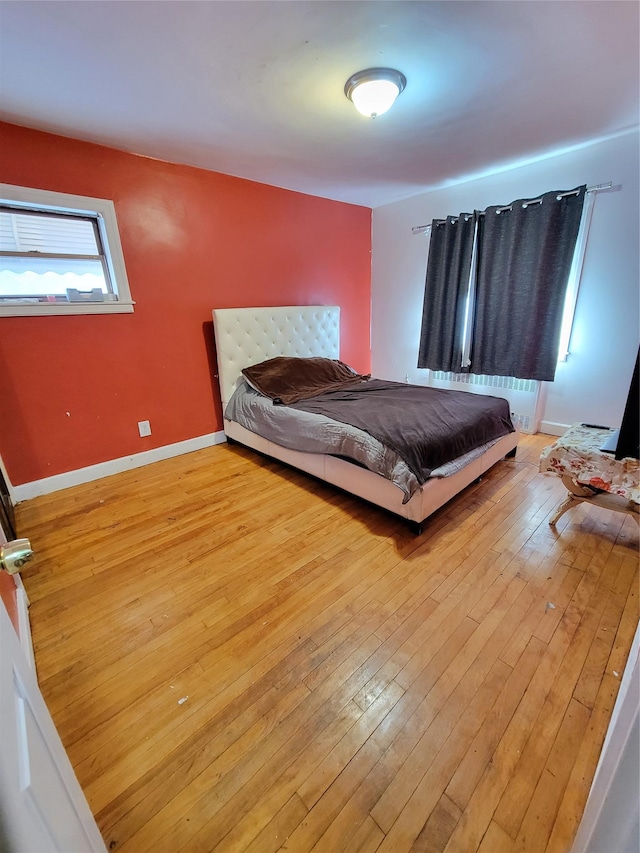 bedroom featuring radiator heating unit, baseboards, and light wood finished floors