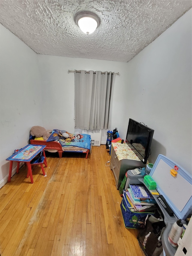 bedroom with a textured ceiling, light wood-style flooring, and radiator heating unit