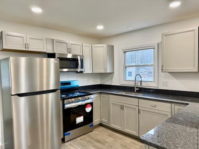 kitchen with light wood-type flooring, appliances with stainless steel finishes, sink, and dark stone counters