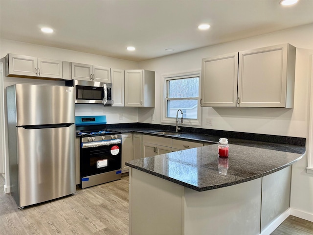 kitchen featuring appliances with stainless steel finishes, dark stone counters, sink, kitchen peninsula, and light hardwood / wood-style flooring