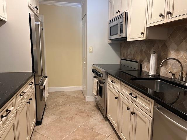 kitchen featuring crown molding, appliances with stainless steel finishes, sink, light tile patterned floors, and dark stone countertops