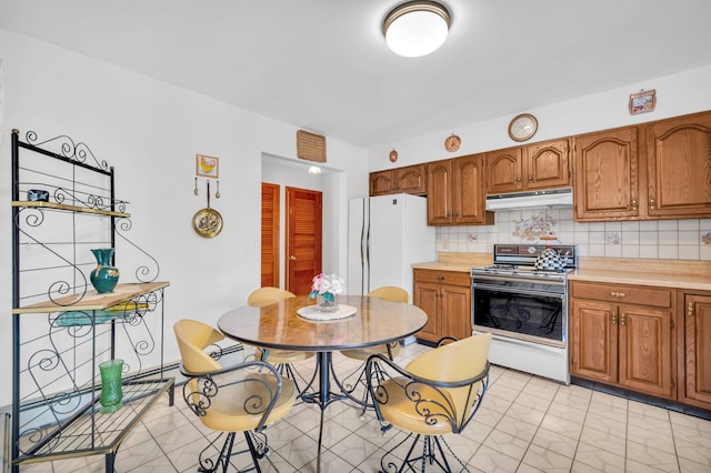 kitchen featuring gas range, light countertops, freestanding refrigerator, and under cabinet range hood