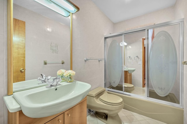 full bath with vanity, tile patterned flooring, tile walls, toilet, and combined bath / shower with glass door