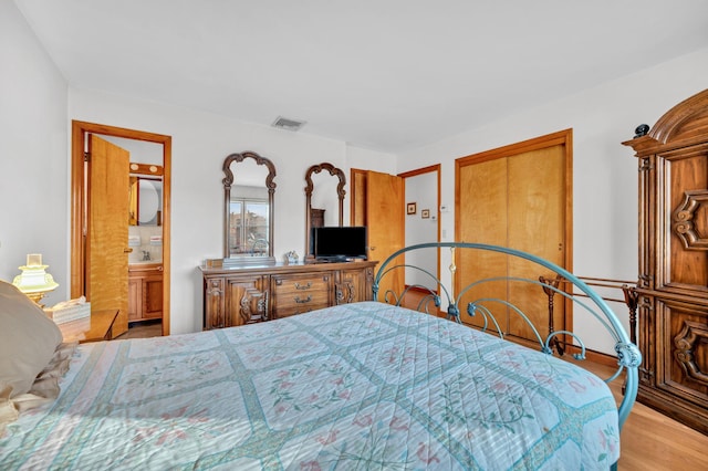 bedroom with visible vents, ensuite bathroom, and wood finished floors