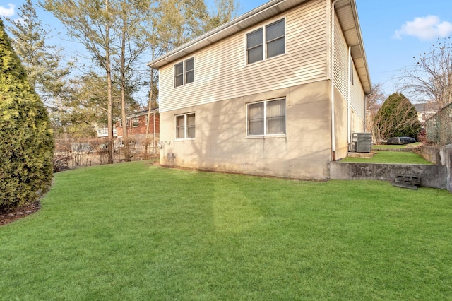 rear view of house with central AC unit, a lawn, and fence