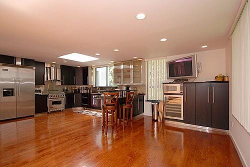 kitchen featuring built in appliances, hardwood / wood-style flooring, decorative backsplash, wall chimney exhaust hood, and beverage cooler