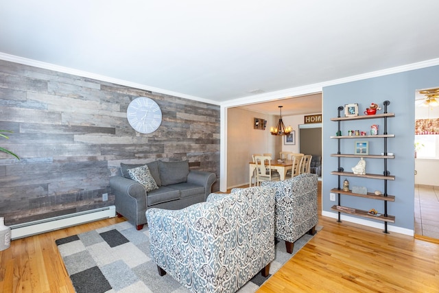 living room featuring baseboard heating, wooden walls, ornamental molding, a notable chandelier, and hardwood / wood-style flooring