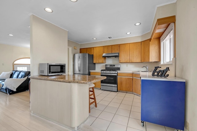 kitchen with a breakfast bar area, under cabinet range hood, stainless steel appliances, open floor plan, and light countertops