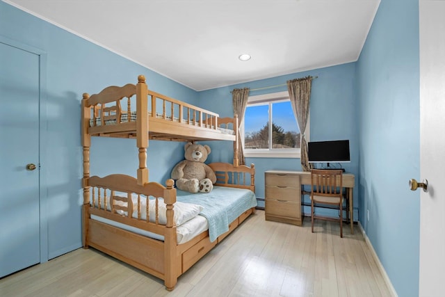 bedroom with light wood-type flooring, a baseboard heating unit, and baseboards