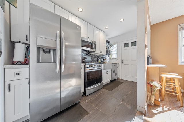 kitchen featuring decorative backsplash, stainless steel appliances, dark tile patterned floors, and white cabinets