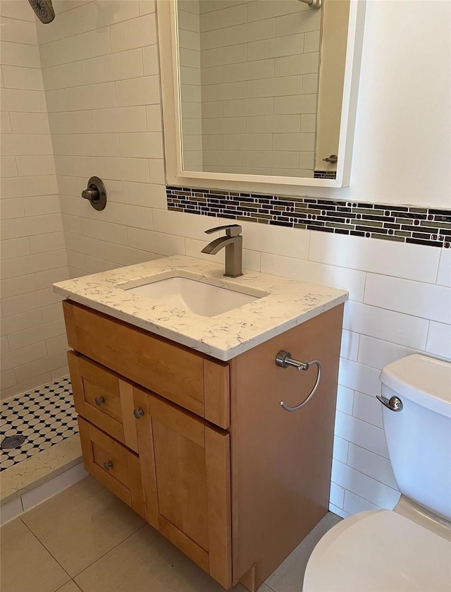 bathroom featuring toilet, a tile shower, tile walls, tile patterned floors, and vanity