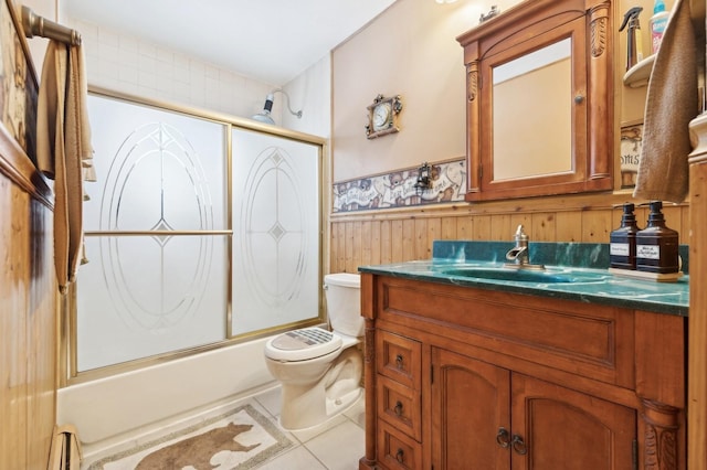 full bathroom featuring toilet, bath / shower combo with glass door, vanity, wooden walls, and baseboard heating