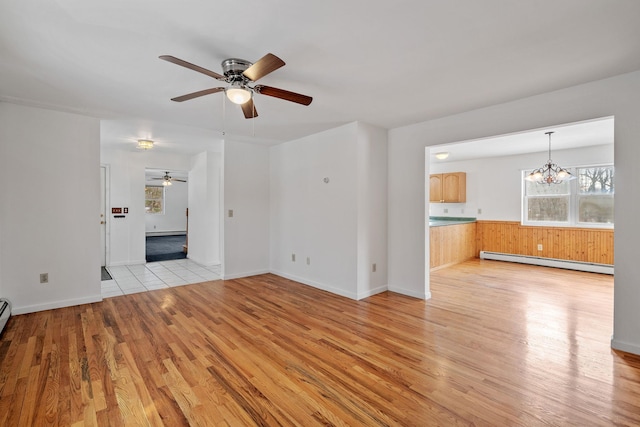 unfurnished living room with ceiling fan with notable chandelier, baseboard heating, and light hardwood / wood-style floors