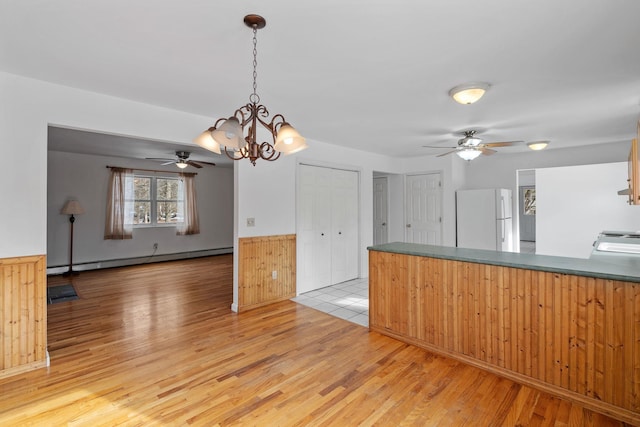 kitchen featuring light hardwood / wood-style flooring, hanging light fixtures, white fridge, a baseboard radiator, and wood walls